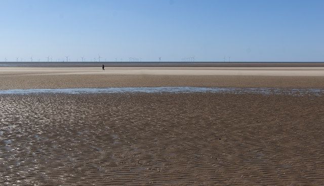 A single walker on the beach with a wind farm in the distance