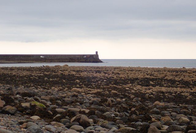View across a boulder beach towards the seaward end of the breakwater at Gyles Quay